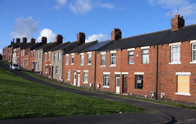Sloping terrace of red-brick miners' houses on Angus Street, Easington Colliery, with a grass bank in front