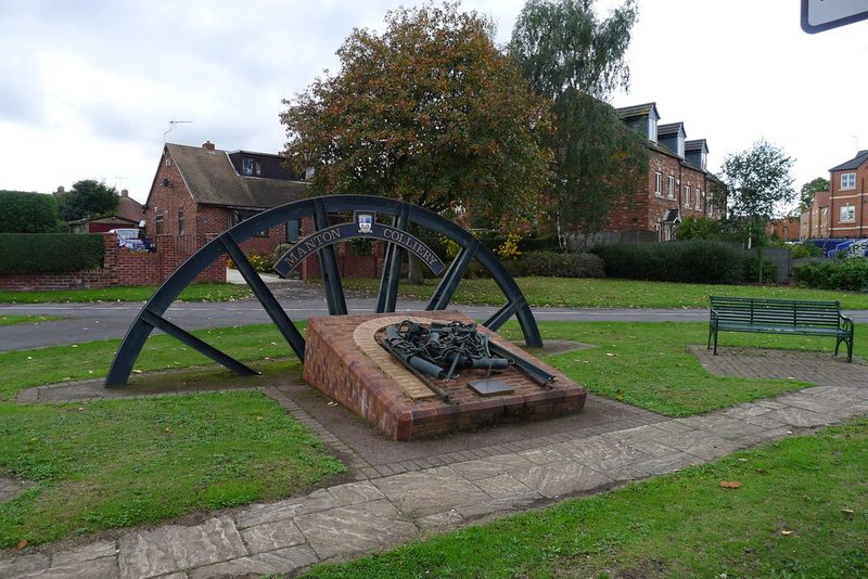 A half pit wheel lettered Manton Colliery standing over a brick plinth of mining relics on a green.
