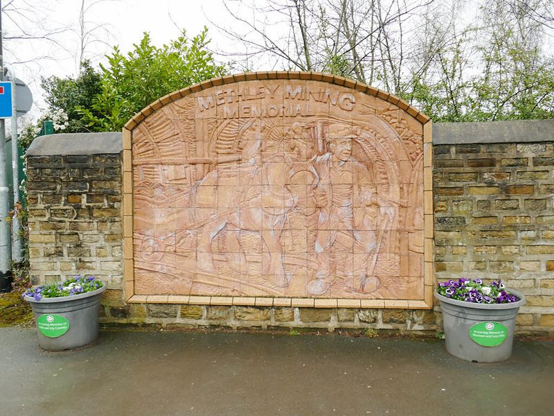 An arched terracotta relief of a miner leading a pit pony, titled Methley Mining Memorial, set into a brick wall.