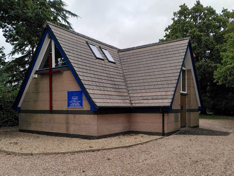 A low modern brick church with a pitched roof and a small bell turret at the end of a village street.