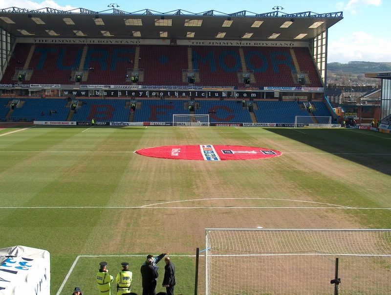 A modern all-seated football stand with a roof, seen across the pitch at Turf Moor.