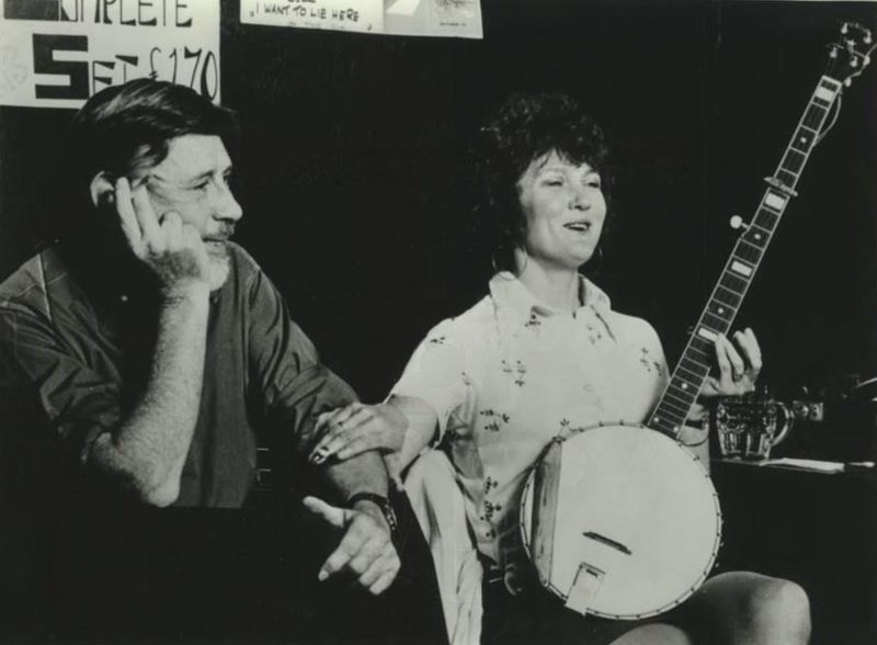 Black-and-white photograph of Ewan MacColl and Peggy Seeger seated at a club, Seeger holding a banjo.