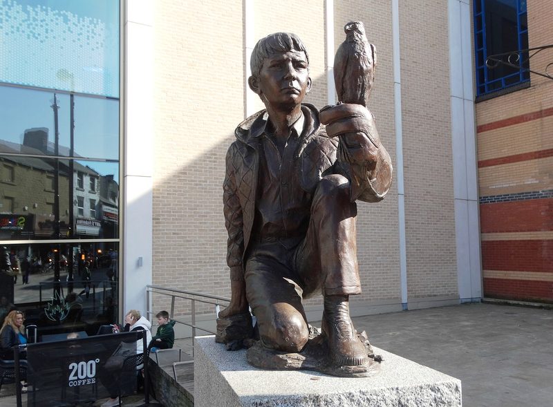 Bronze statue of a kneeling boy with a kestrel on his gloved hand, on a stone plinth outside a town-centre building.