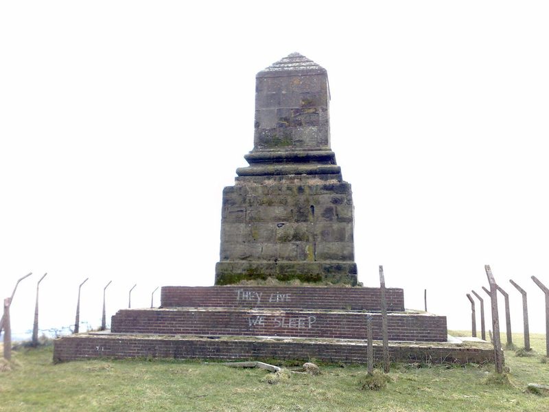 A tall stone monument on a grassy hilltop.