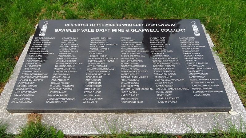 Stone memorial with a carved miner and inscription commemorating miners lost at Glapwell Colliery, standing on grass.