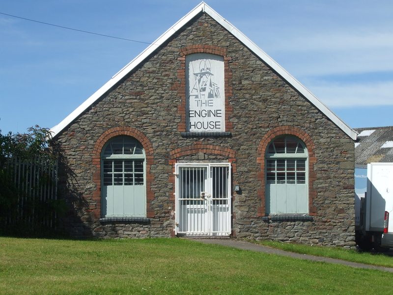 A stone gable-ended engine house with brick-arched windows and a sign reading The Engine House.