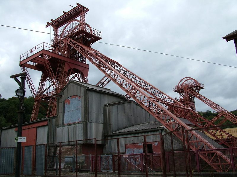 Two red steel headframes and winding-house buildings under a grey sky.