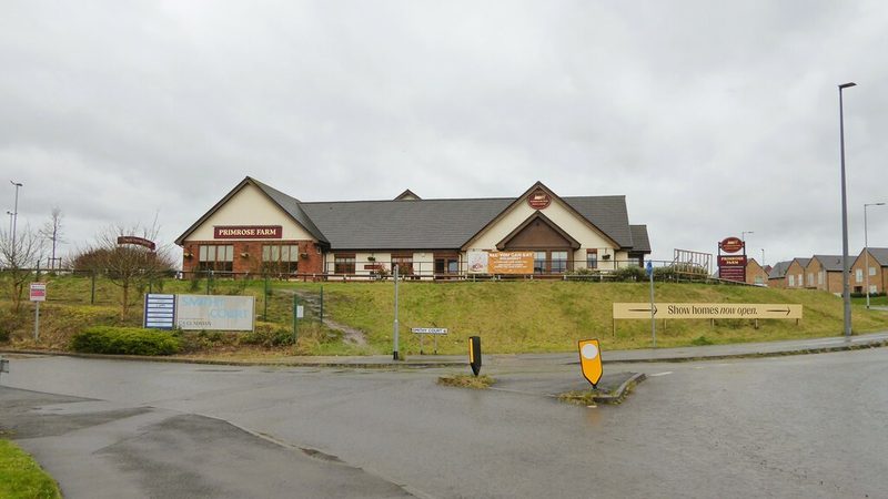 A new single-storey pub building on a grassy bank beside a road junction, with houses behind.