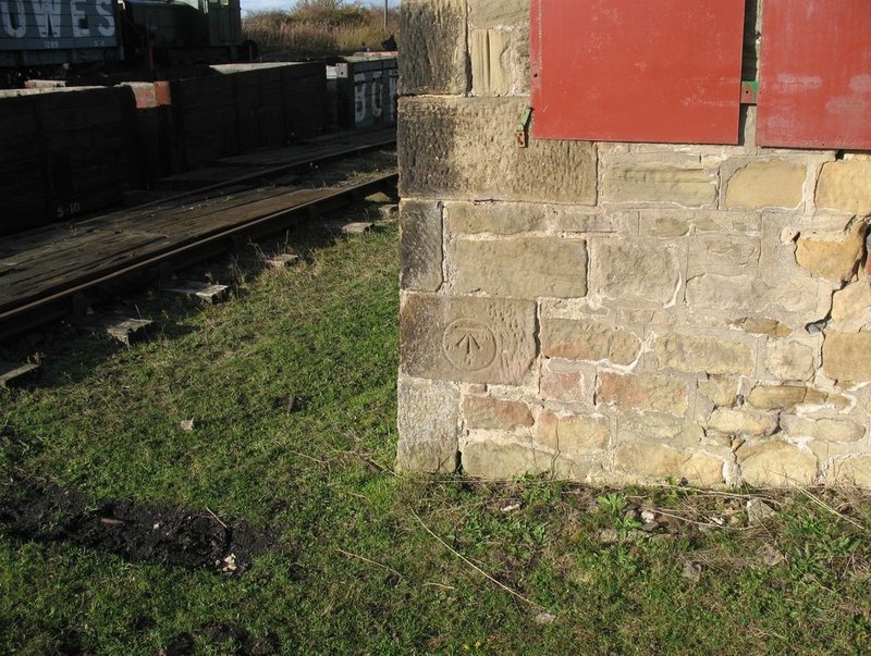 The sandstone corner of the old colliery workshop, with red doors and railway wagons behind.