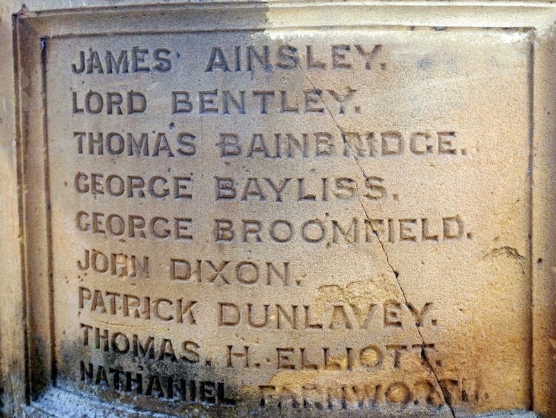 A close view of carved names on a sandstone memorial panel, beginning James Ainsley and running down through George Broomfield, John Dixon and Thomas H. Elliott.