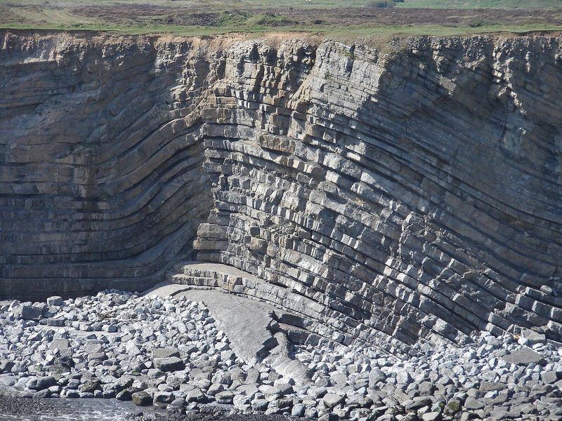 A sea cliff of thinly bedded limestone in which the beds bend sharply up and over into an arch.