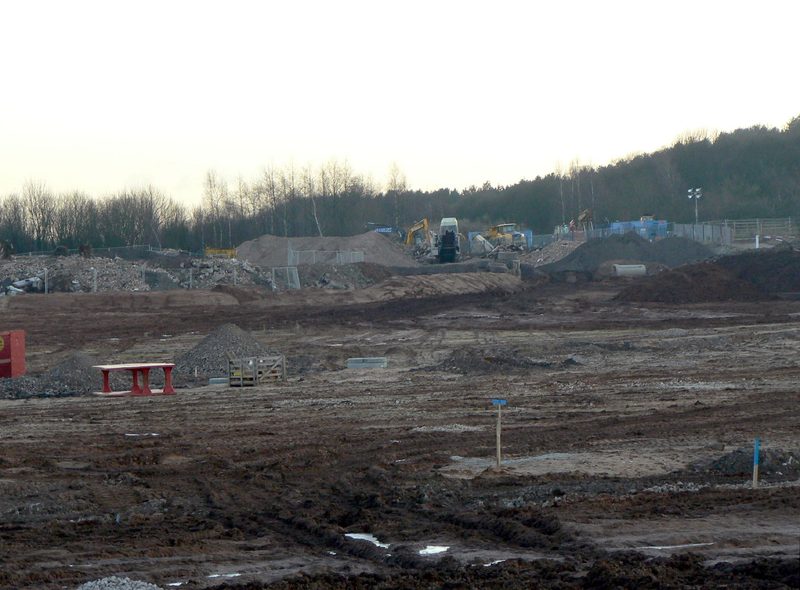 The surviving steel headframe and derelict colliery buildings standing on a largely cleared site of rubble and rough ground.