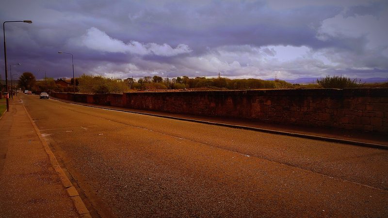 The long boundary wall of the former Bathville brick and fireclay works standing along an empty cleared site of rough ground.