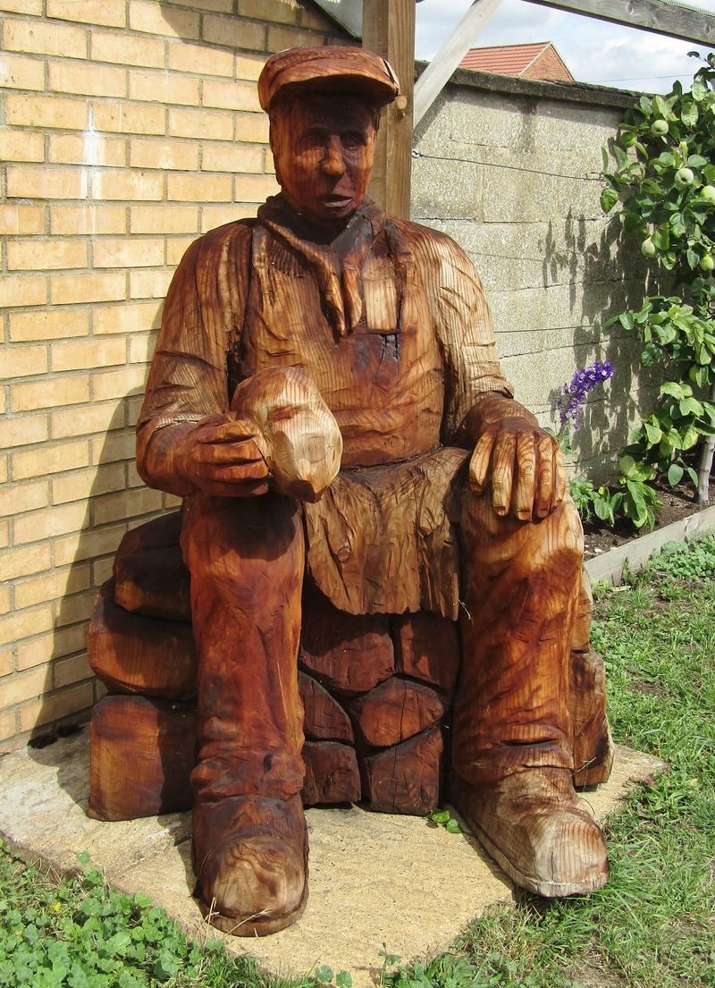 A carved wooden figure of a flint knapper at work, standing in Brandon
