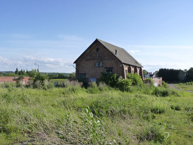 A gabled brick winding house with buttressed side walls standing in rough grassland.