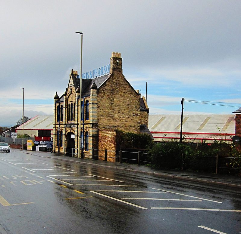 The restored yellow-brick office and weigh house of the Harris and Pearson firebrick works on Brettell Lane, with blue brick bands, terracotta dressings and an arched carriageway through the centre bay.