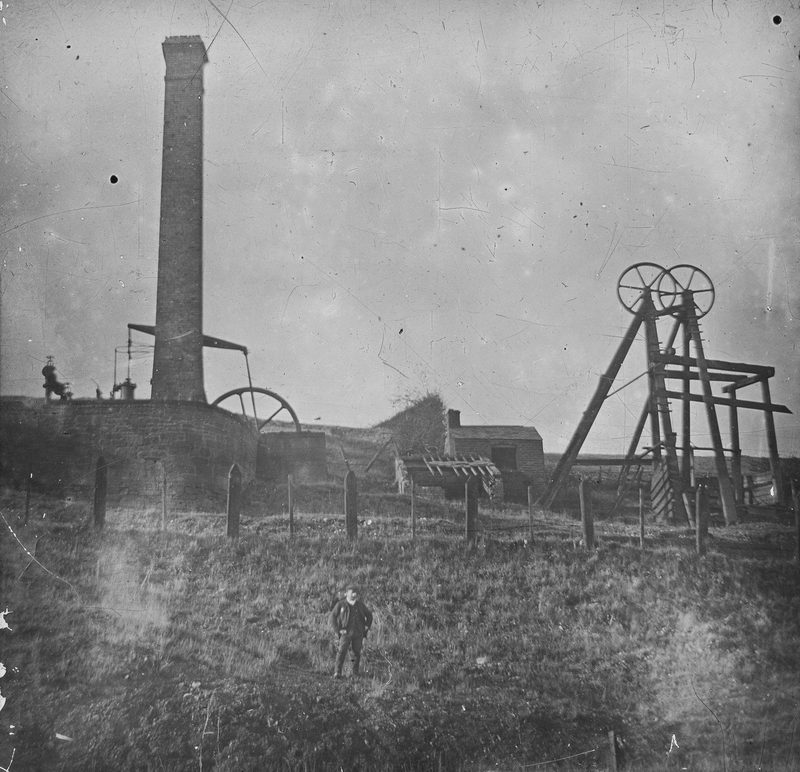 A black and white photograph of old colliery and works buildings at Brymbo, with headgear and spoil on the hillside.