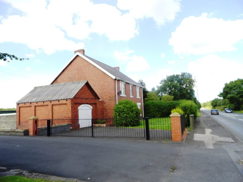 A red-brick house with a garage behind railings beside a main road