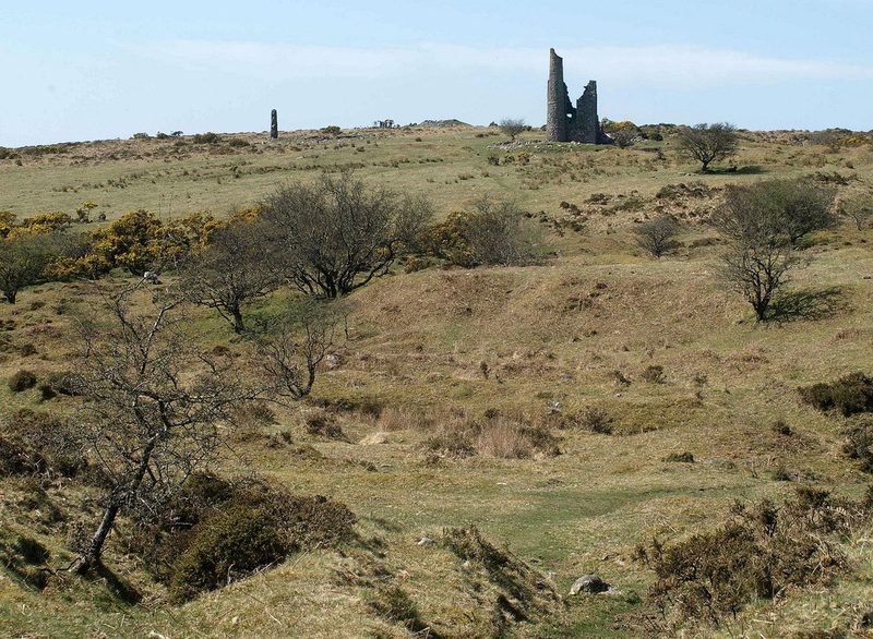 A tall stone chimney beside the low ruined walls of an engine house on open moorland.