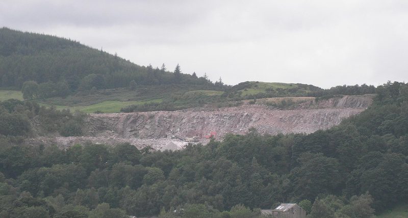 The grey worked face of Craignair granite quarry cut into the hillside above Dalbeattie, with trees along its foot.