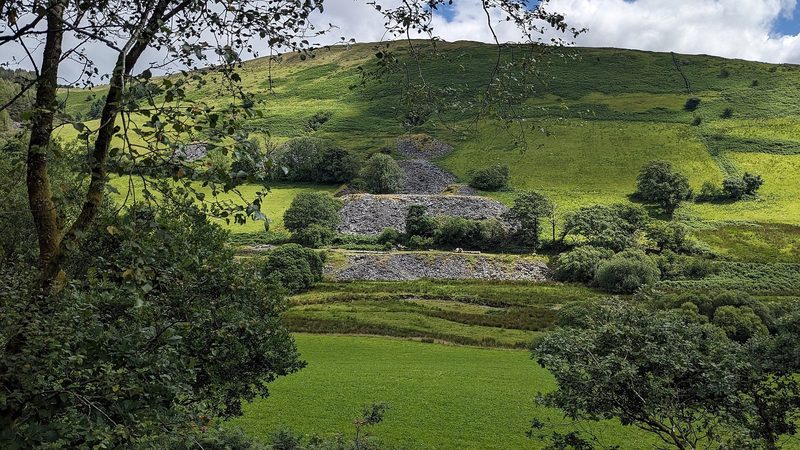 Grey slate waste tips of Cymerau Quarry spilling down the hillside above the Nant Ceiswyn.