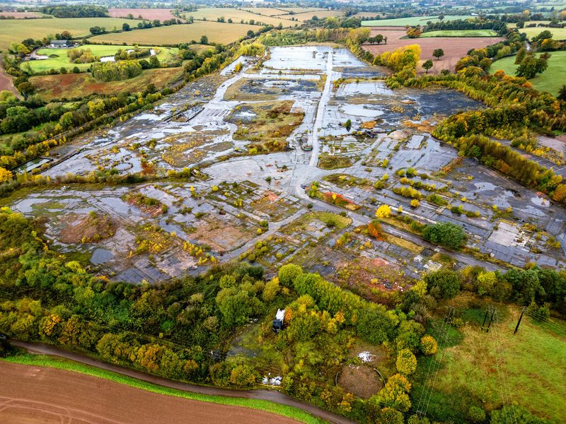 An aerial view of a large expanse of broken concrete and pools of water surrounded by autumn trees and farmland.