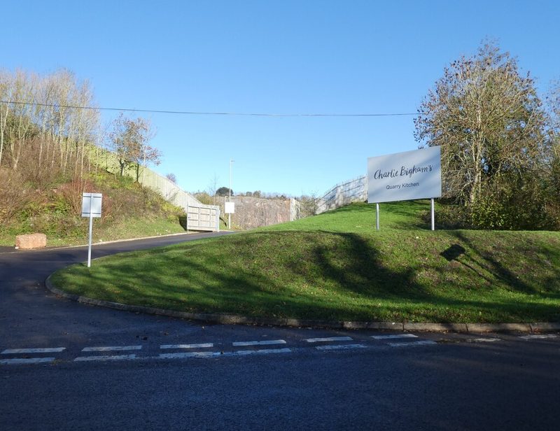 The road entrance to Dulcote Quarry, with the cut hillside and trees rising behind.