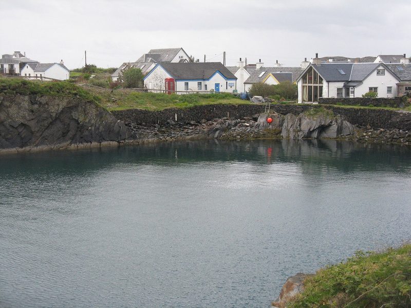 Still green water filling a flooded slate quarry, with the white buildings of the Easdale Island Folk Museum beside it