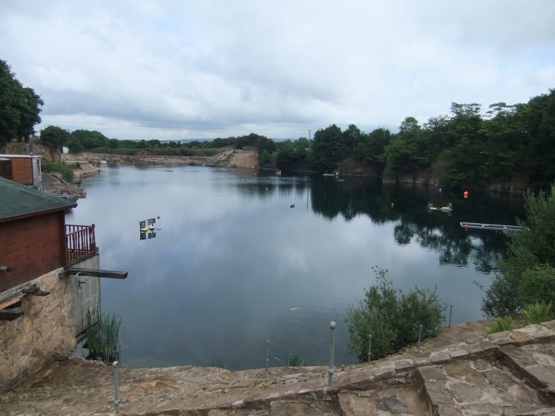 The flooded floor of Eccleston Quarry seen along its length from the car park, still green water held between wooded rock faces