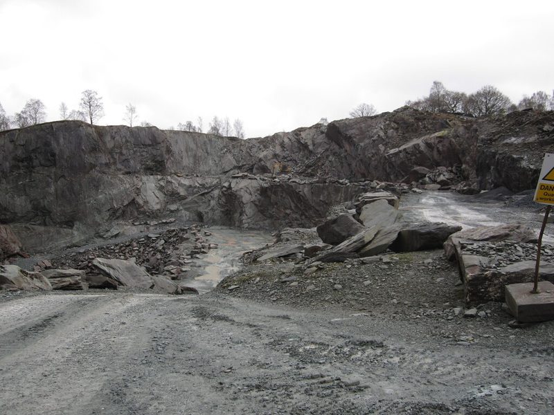 The open slate workings at Elterwater, a stepped grey-green face cut into the fellside with waste runs below it.