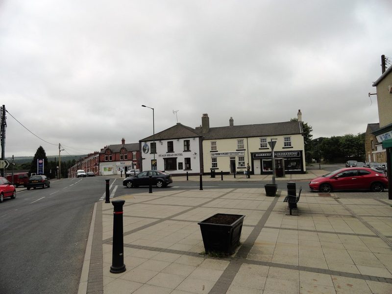 A village street corner with a hotel, barber's and shops, and brick terraces running away downhill