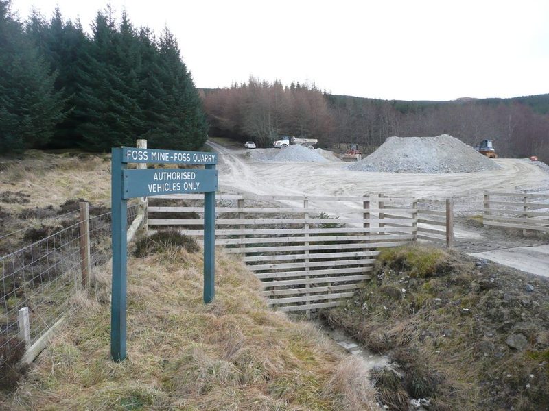 The Foss Mine and Foss Quarry sign at the mine entrance, with pale stockpiles of rock and conifer forest behind.