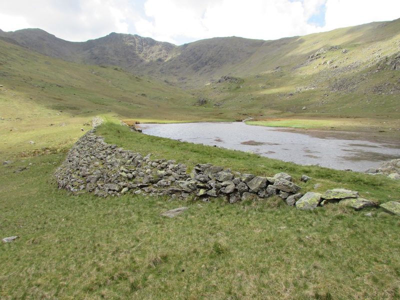 The rubble-stone dam of Greenburn Reservoir, built to power the mine's machinery, curving across the valley below the fells.