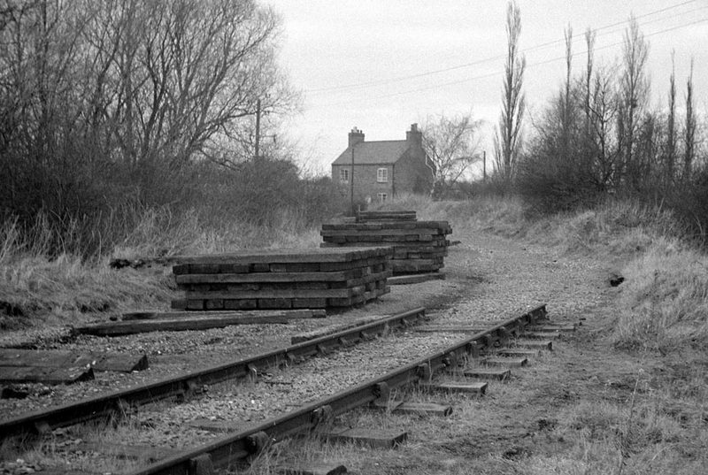 A single disused railway track curving away through winter fields towards trees