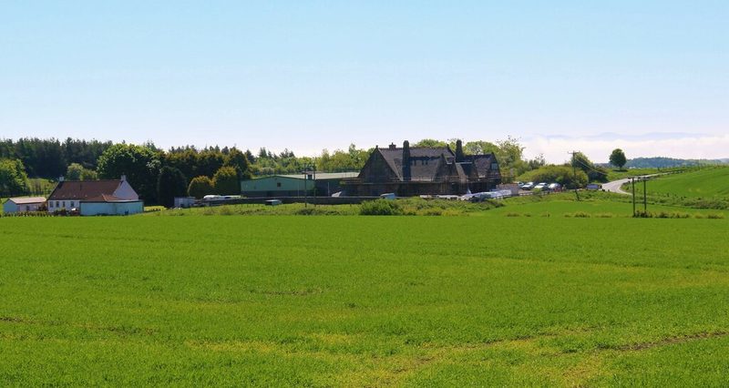 Farm buildings and a former school beyond a green field at Chant Houses, where a Halbeath Colliery spoil heap once stood.