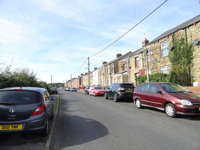 A long stone terrace of pre-1914 miners' houses along a village street lined with parked cars