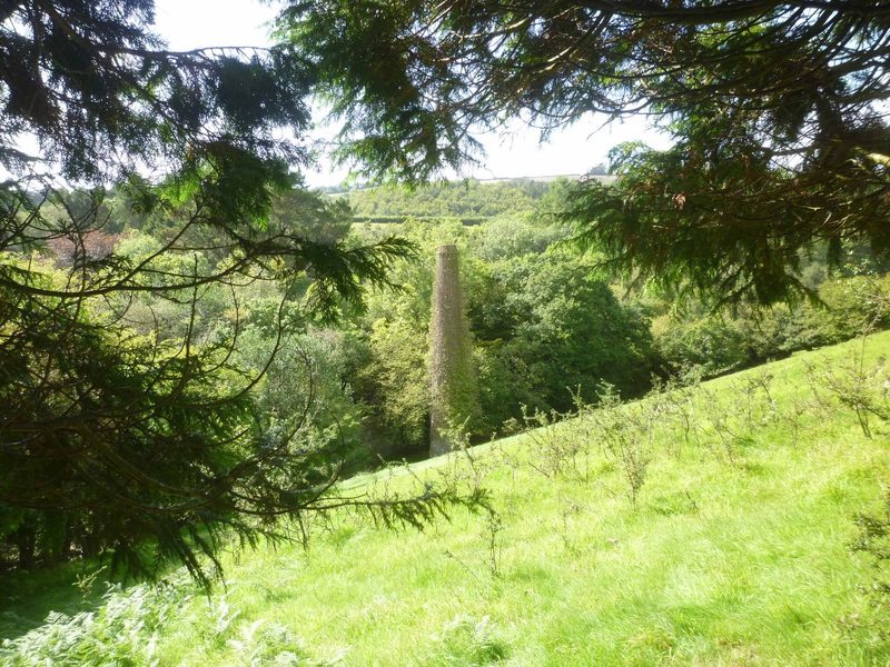 The stone chimney of Herodsfoot Mine standing among trees in the valley.