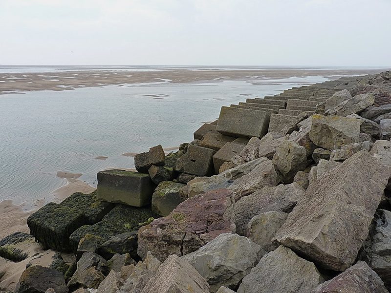 Rows of large weathered concrete blocks and limestone rubble sloping down to the tidal sands of the Duddon estuary.