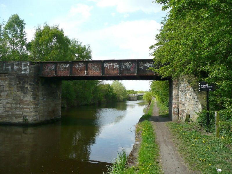 A graffiti-covered steel girder bridge on stone abutments spanning a canal, with a towpath and a sign reading 'Bridge 39 Ingham Colliery', 2011
