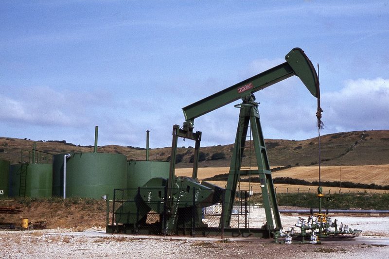 A beam pumping unit, or nodding donkey, standing in a fenced compound on the clifftop above Kimmeridge Bay, with the sea beyond.