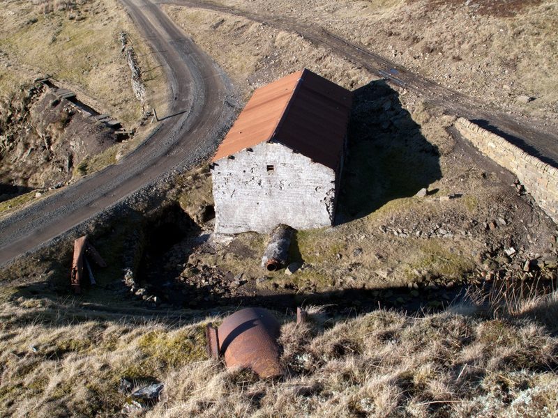 A small stone building with a pitched roof standing on rough moorland grass beside spoil.