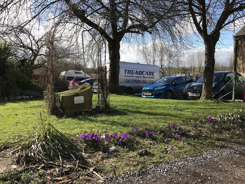 The Minnie Pit memorial garden at Halmer End, with a memorial stone, planting and a pit wheel beside the road