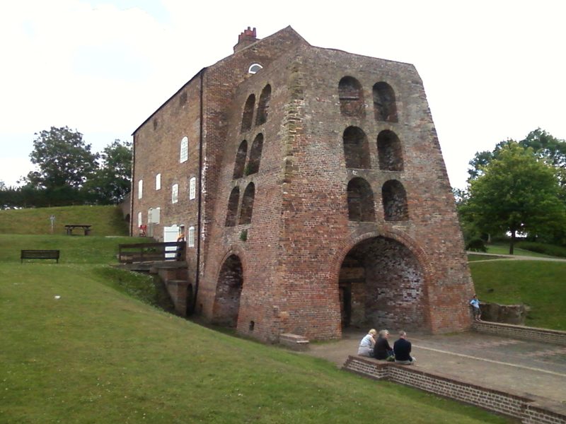A tall brick blast furnace building with arched openings and a bridge house, standing beside the restored Ashby Canal at Moira.