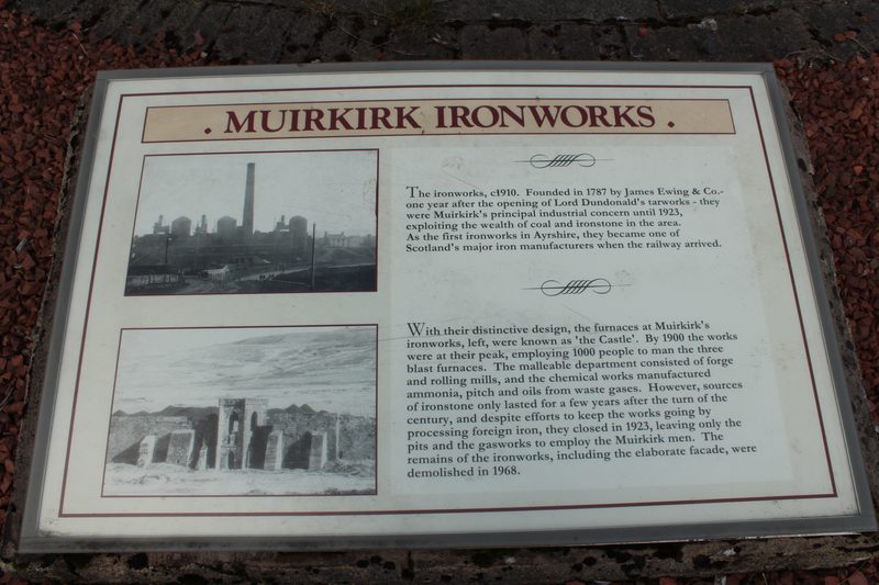 Stonework surviving from the Muirkirk ironworks, laid out within the village heritage garden, with grass and moorland behind.