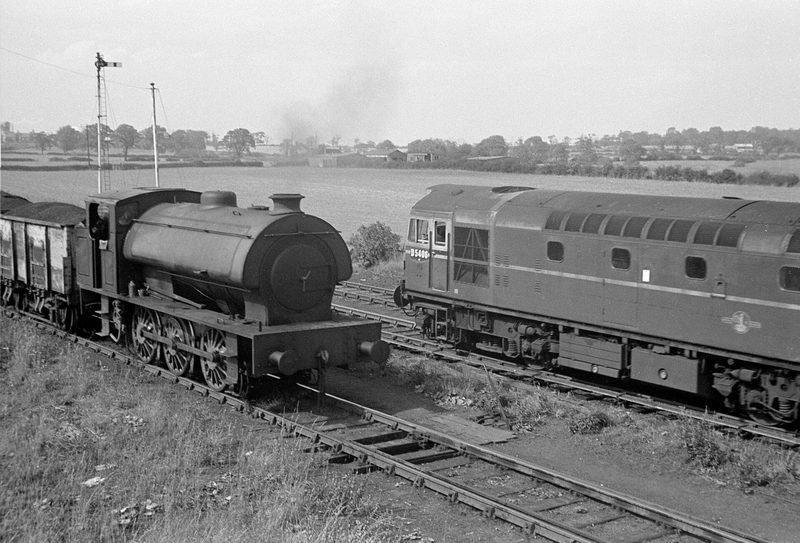 A saddle tank locomotive bringing a train of loaded coal wagons from Nailstone Colliery into the exchange sidings at Bagworth, with a main line diesel passing.