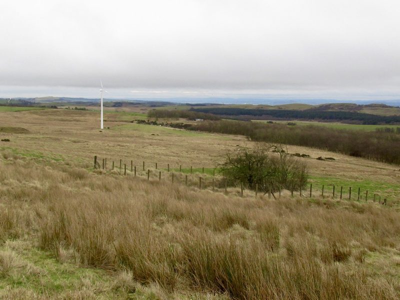 A square fence of posts and wire around an old mineshaft in rough winter grassland on a hillside above Steelend, with hills beyond