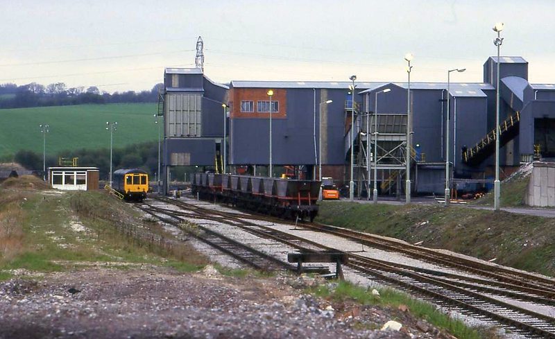 Grey coal-handling buildings and conveyors beside railway sidings, with a diesel train on one track.