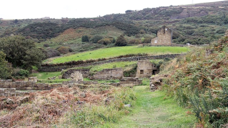 Masonry foundations and walls of the alum works on the clifftop terrace at Ravenscar, with the sea beyond.