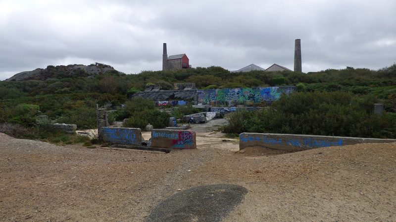The stone engine house and chimney of Penhall's Mine standing on open cliff ground above St Agnes, with the sea beyond.