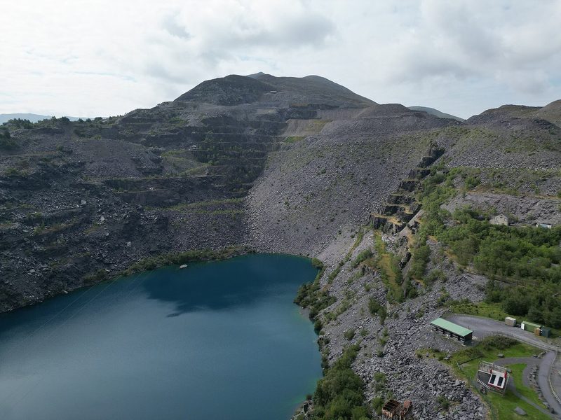 Aerial view of the terraced galleries and grey slate tips of Penrhyn Quarry near Bethesda, with the mountains of Eryri beyond.